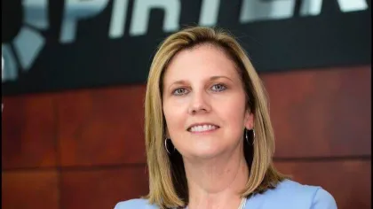 Professional woman in blue Pirtek uniform posing confidently in front of company logo indoors.