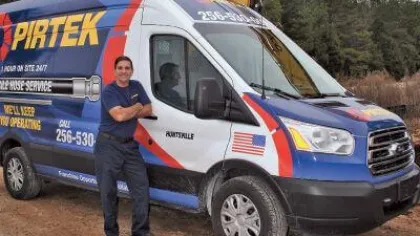 Technician stands next to blue and white PIRTEK service van with American flag and company branding outdoors.