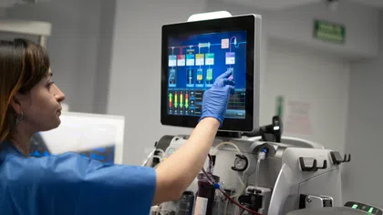 Medical technician in blue scrubs using touchscreen to operate advanced dialysis machine in hospital setting