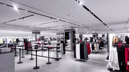Modern clothing store interior with racks displaying various apparel, bright lighting, and spacious layout.