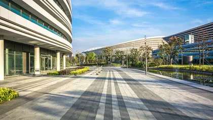 Modern curved office buildings along a wide paved walkway with trees and a reflecting pond under a clear blue sky