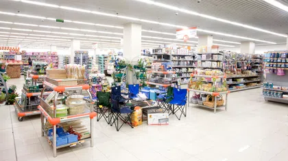 Bright, spacious store interior with shelves stocked with various household goods, camping chairs, and storage items.