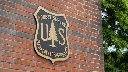 US Forest Service Department of Agriculture emblem mounted on a red brick wall with green trees in the background
