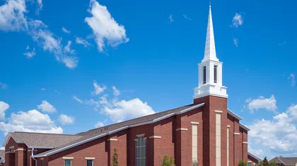 Red brick church with white steeple under blue sky with scattered white clouds
