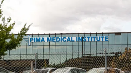 Exterior of Pima Medical Institute building with reflective glass windows and parked cars in front under cloudy sky
