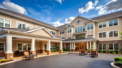 Modern senior living community building with outdoor seating, landscaped gardens, and a clear blue sky.