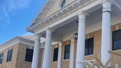 Brick building with large white classical columns and a blue sky background under renovation.