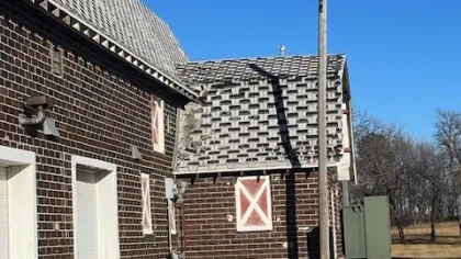 Brick barn with white garage doors and patterned roof under clear blue sky in rural setting