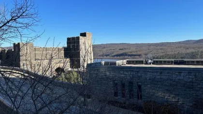 Stone castle-like building with train cars on tracks and bare trees under a clear blue sky.