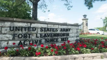 Stone sign with black letters reading United States Army Fort Leavenworth active since 1827 amid red flowers.