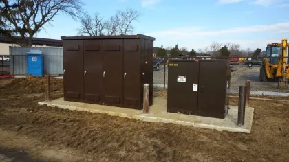 Brown electrical utility cabinets on concrete slab at a construction site with machinery and fencing in background