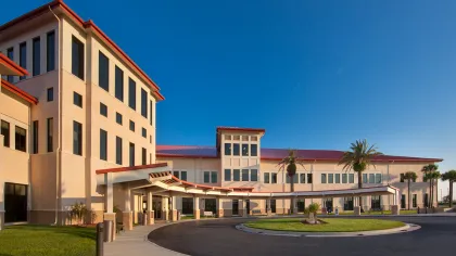 Modern beige medical building with red roof and circular driveway under a clear blue sky.