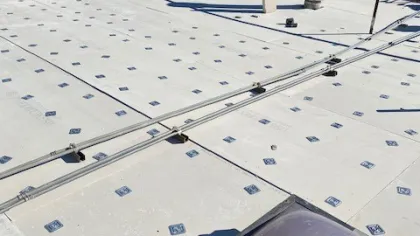 Flat rooftop under construction with insulation panels and workers installing metal grates and wiring.