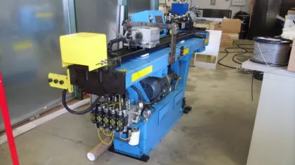 Blue industrial machine with yellow panel used for manufacturing in a workshop with concrete floor and equipment around.