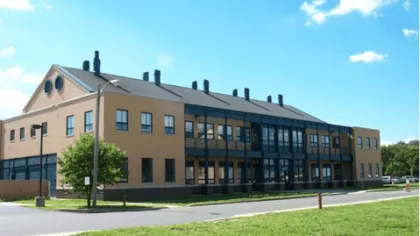 Large beige and black two-story building with multiple windows and chimneys under a bright blue sky