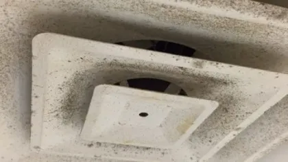 Close-up of a dirty, dust-covered white ceiling air vent with visible grime buildup.