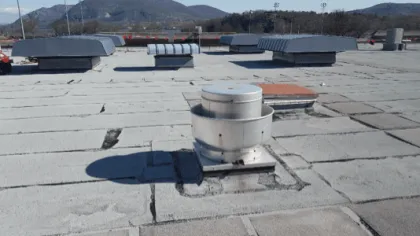 Flat commercial rooftop with HVAC vents and mountains in the background under clear blue sky.