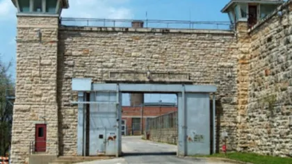 Stone prison entrance with watchtowers and metal gates under a blue sky.