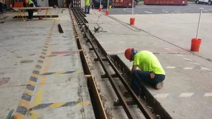 Workers in safety gear installing metal rails in a warehouse loading dock area with construction materials nearby.
