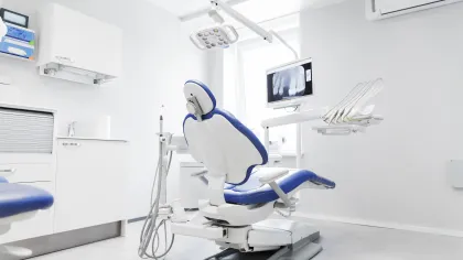 Modern, clean dental clinic with a blue dental chair, equipment, and an X-ray displayed on screen.