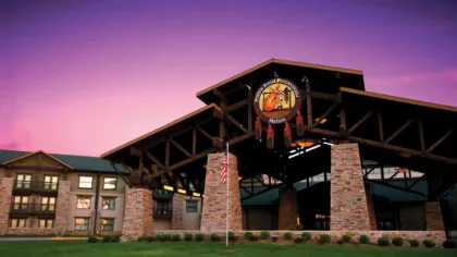 Stone and wood lodge entrance with a circular sign and American flag at sunset with a purple sky.