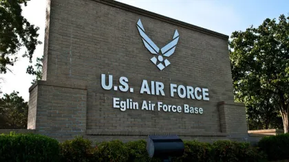 Entrance sign of U.S. Air Force Eglin Air Force Base with emblem on brick wall surrounded by trees.