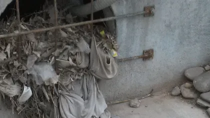 Clogged concrete drain filled with debris, leaves, plastic, and fabric blocking water flow
