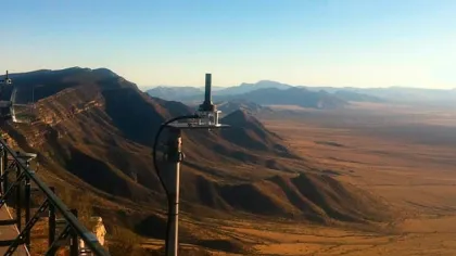 Aerial view of arid mountains and desert landscape under clear blue sky with scientific equipment on a balcony.