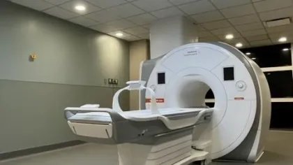 Modern MRI machine in a clean medical room with ceiling panels showing sky and tree designs.