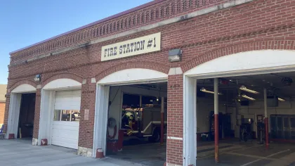 Brick fire station with open bays and a fire truck inside under a sign reading Fire Station #1.