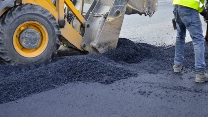 Construction workers using machinery to lay and spread fresh asphalt on a road surface.