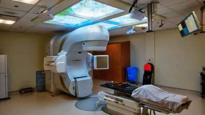 Modern radiation therapy room with large linear accelerator machine and patient treatment table under bright ceiling lights