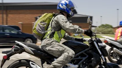 Motorcyclist wearing blue helmet and safety vest rides black motorcycle in urban setting with backpack.