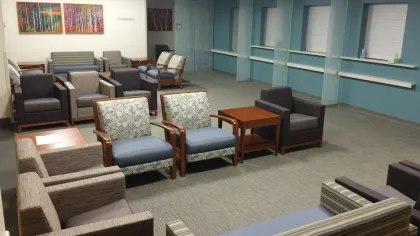Spacious hospital waiting room with various armchairs, couches, wooden tables, and artwork on walls.