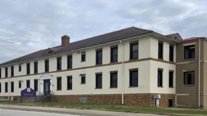 Two-story institutional building with cream and brown walls under a cloudy sky on a quiet street.