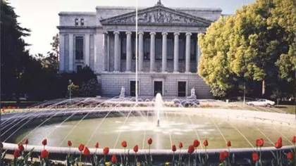Historic neoclassical building with columns, central fountain, and red tulips in the foreground under daylight.