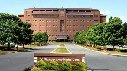 Front view of Womack Army Medical Center building with surrounding trees and entrance road under clear sky