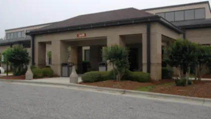 Modern office building entrance with large pillars, landscaped bushes, and a paved driveway on a cloudy day
