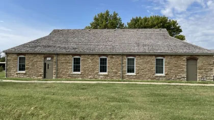 Historic stone building with wooden shingle roof and multiple windows under a blue sky with scattered clouds.