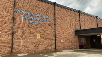 Brick exterior of Turtle Mountain Elementary School with blue signage under a cloudy sky.