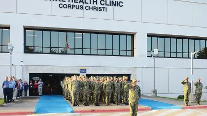 Uniformed Navy personnel standing in formation outside Naval Health Clinic Corpus Christi building during a ceremony.