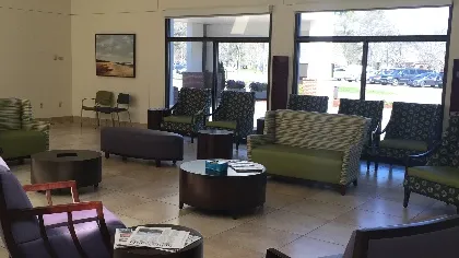 Modern waiting room with various patterned chairs, coffee tables, large windows, and tiled floor.
