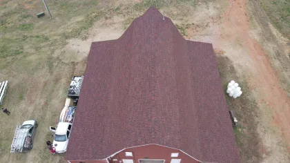 Aerial view of a brown-roofed barn surrounded by vehicles and grassy land with dirt paths.