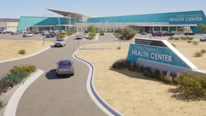 Modern Pueblo Pintado Health Center building with parking lot and desert landscape under clear sky.