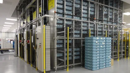 A large automated storage system with blue plastic bins stacked inside metal cages in a clean warehouse.