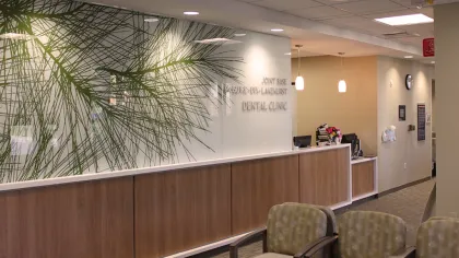 Modern dental clinic waiting area with chairs, wooden reception desk, and frosted glass wall with plant design.
