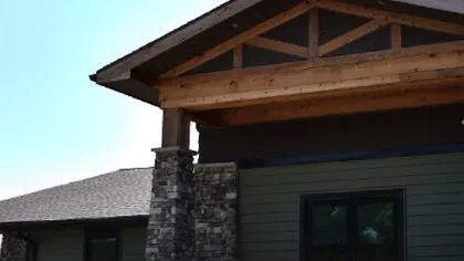 Modern house exterior with stone pillars and wooden roof structure under clear blue sky.