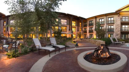 Luxury resort patio with fire pit, lounge chairs, waterfall pool, and landscaped garden at dusk.