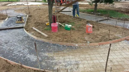 Workers preparing curved concrete pathways with wooden forms and metal rebar in an outdoor construction site with trees.