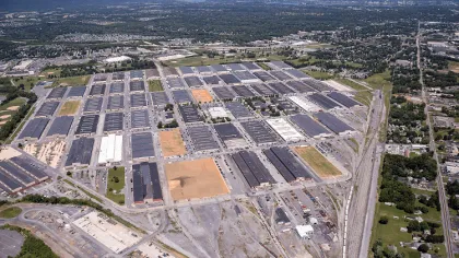 Aerial view of a large industrial complex surrounded by greenery, residential areas, and distant cityscape horizons.